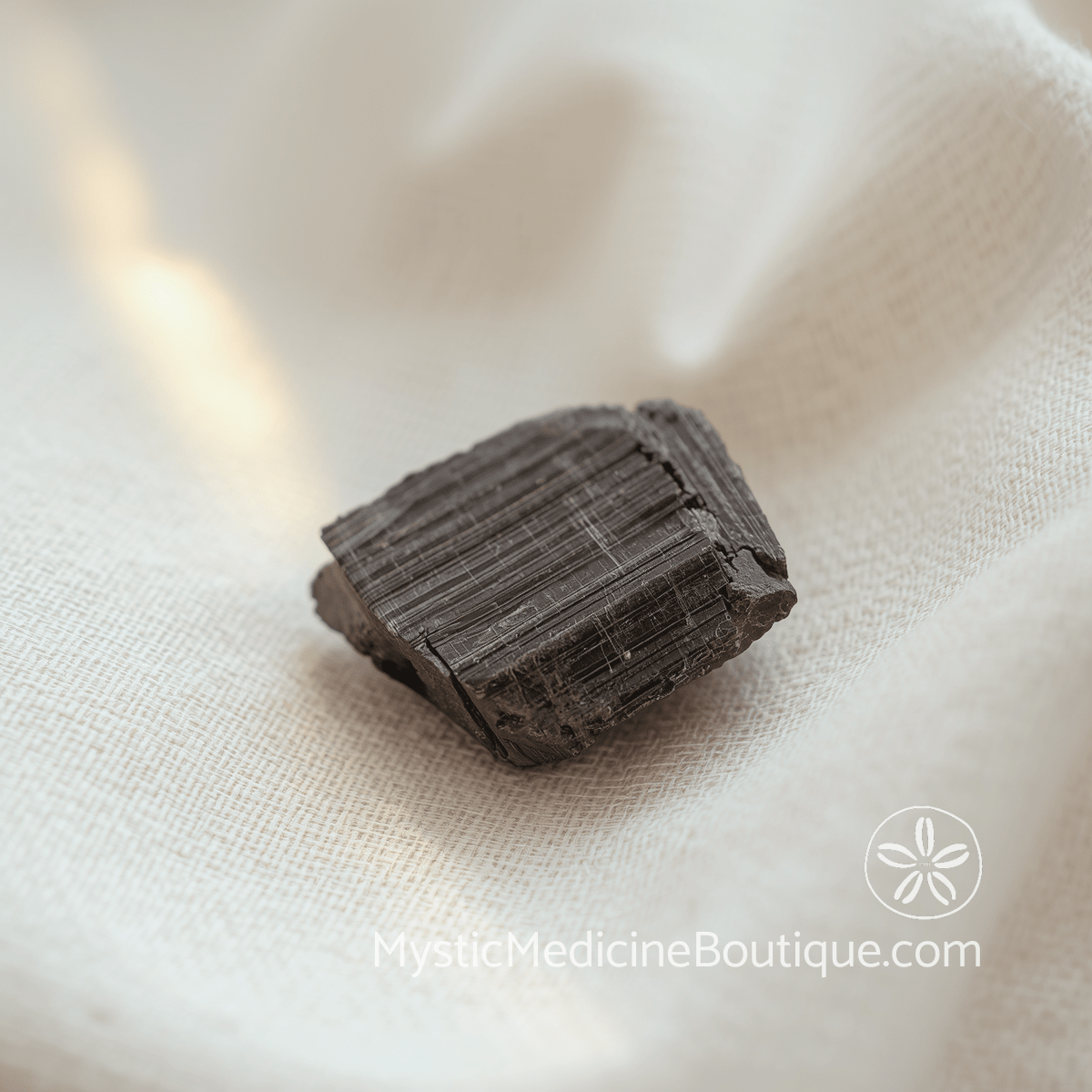 Raw black tourmaline crystal resting on natural cream linen in soft warm light — how to prevent chakra imbalances before spiritual emergency starts, explained by an RN Reiki Master