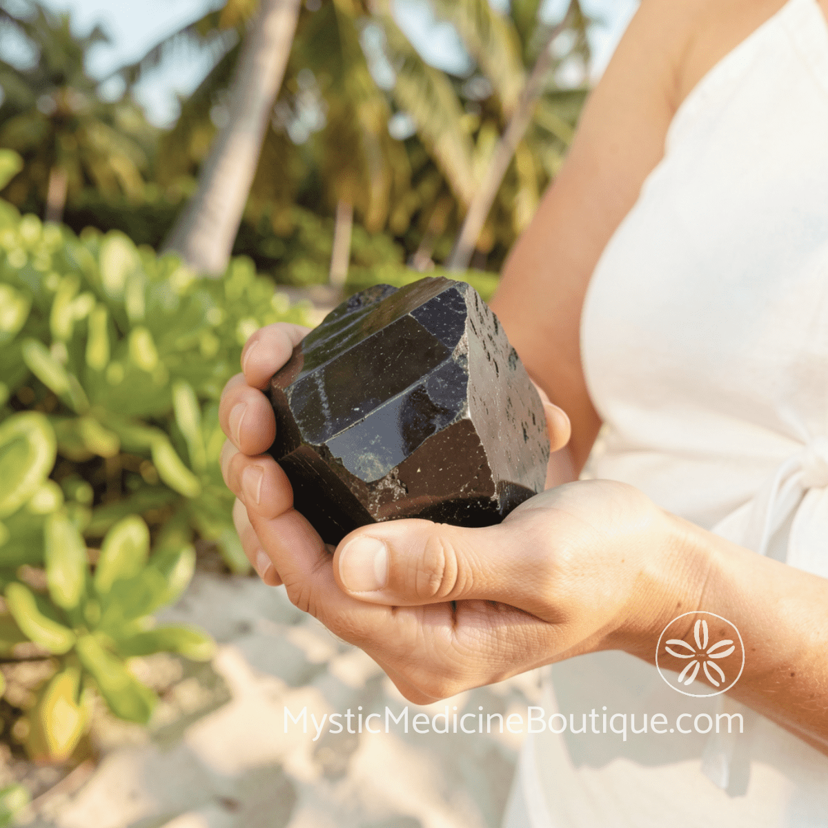 Hands holding large black tourmaline crystal outdoors, how to use crystals during kundalini crisis step-by-step techniques