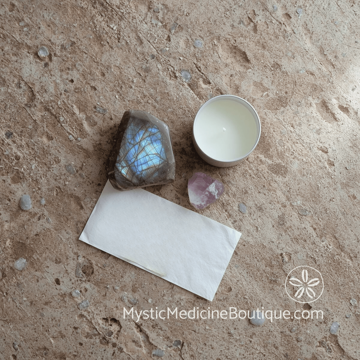 Overhead flat lay of labradorite crystal with blue flash, amethyst point, white candle, and folded paper on natural stone surface, representing long-term mystic practices for maintaining spiritual connection after faith crisis