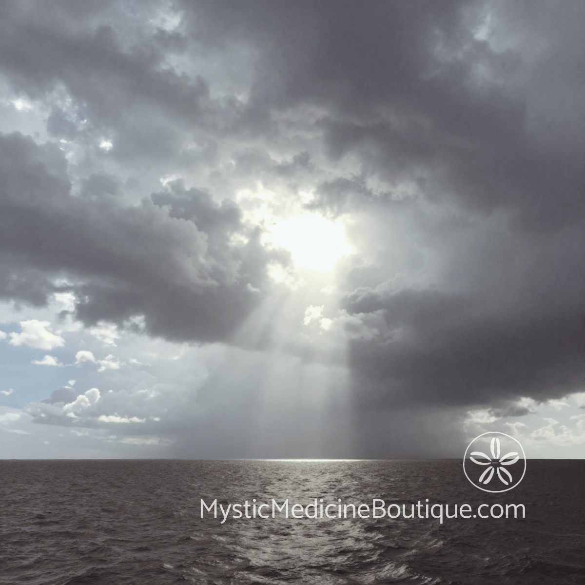 Stormy coastal sky with powerful light rays breaking through dark clouds over open water representing spiritual warfare exhaustion when spirit feels under attack — Mystic Medicine Boutique