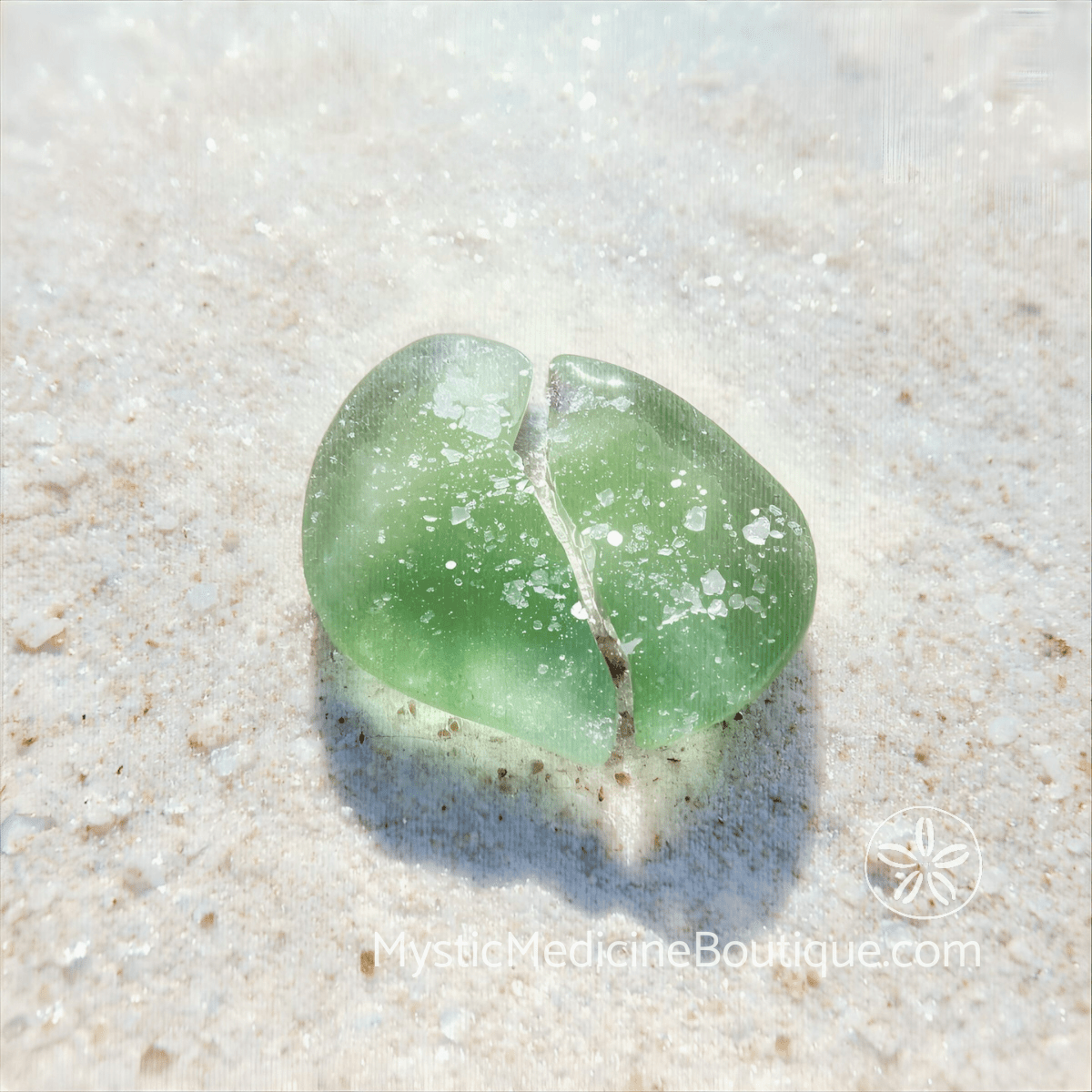 Cracked green sea glass heart on sandy beach representing the shattered trust and existential collapse of spiritual emergency after infidelity discovery