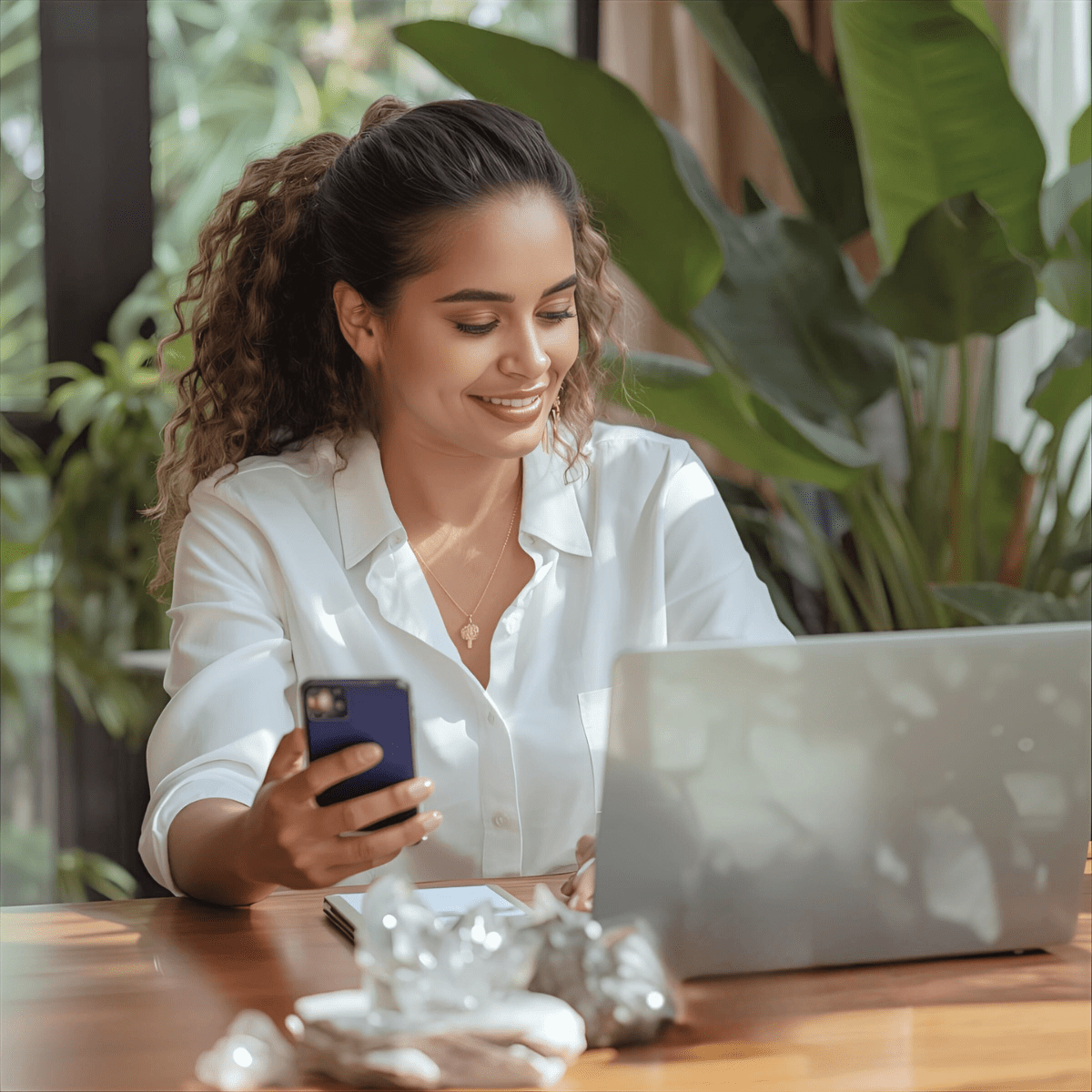 Woman smiling at phone with crystals and laptop amid tropical plants representing the transition from AI spiritual comfort to grounded human support